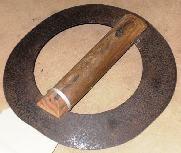 A glover's paring knife, which was used to strip skin. It shows a rectangular piece of wood large enough to fit your hand around it. There is a groove at each end so it can secure a thin circle of sharp metal.