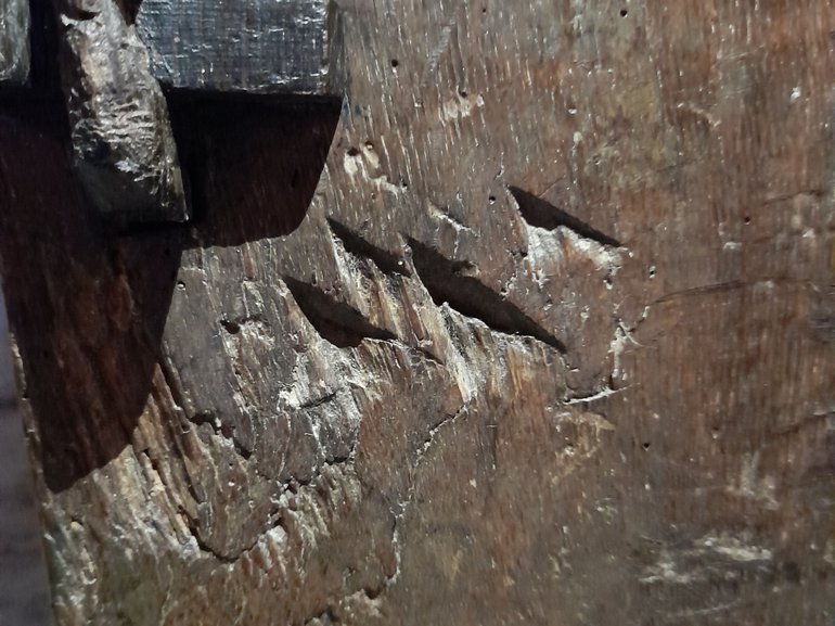 Close-up of four V-shaped marks carved into the dark wood on the side of the grain ark.