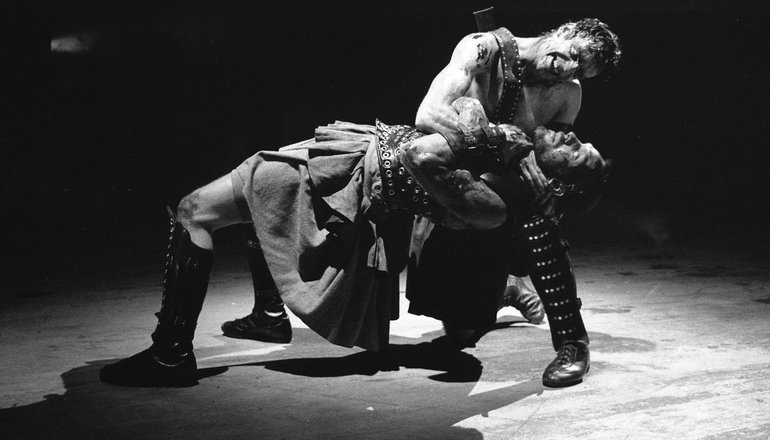 Coriolanus and Aufidius, RSC, 2007. Coriolanus is bent backwards horizontally across the bent knee of the standing Aufidius, who bends his head to look into the face of Coriolanus as he strangles him.