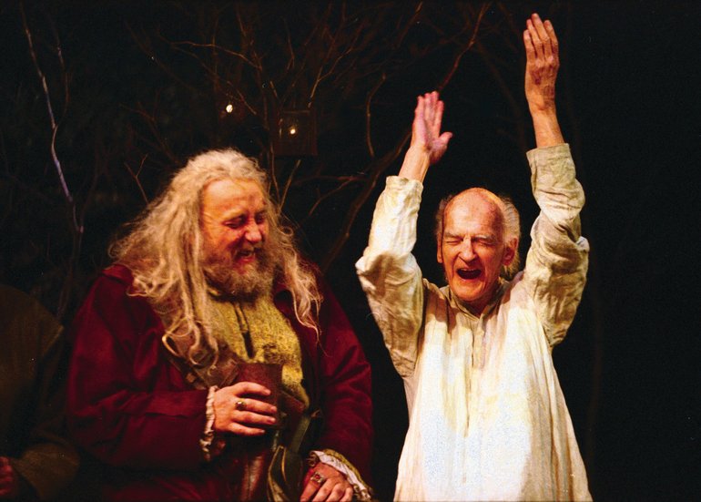 Falstaff has a red gown, shaggy long almost-white hair, and a short brown beard, he holds a tankard. Justice Silence wears a white shirt, and has his hands upraised, his eyes closed, and his mouth open.