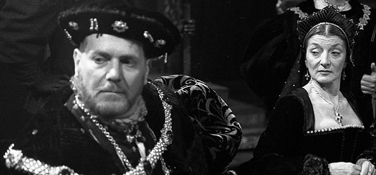 On the right, Queen Katherine, wearing black and an elaborate headdress looks disparagingly at Henry on her right. He, wearing many jewels, leans away from her; he looks stern, but a little troubled.