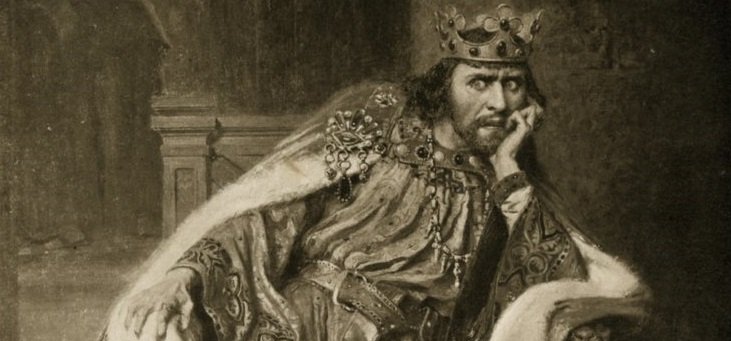 King John Slouches in a chair, his left elbow resting on the arm, his chin in his left hand. His face has an expression combining anger and worry.