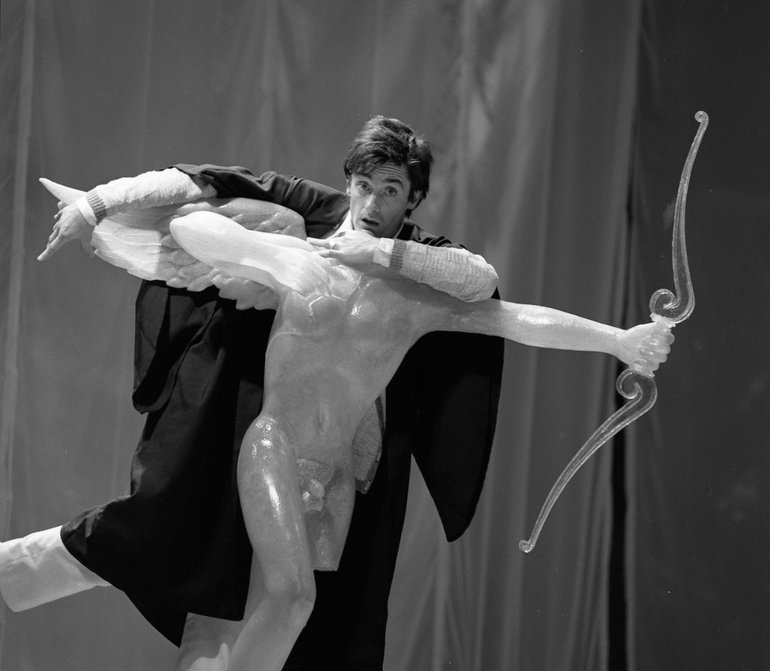 Berowne (in a black gown) using the headless statue of Cupid to hide himself when overhearing his friends breaking their oaths to forswear the company of women in exchange for solitude and philosophy.