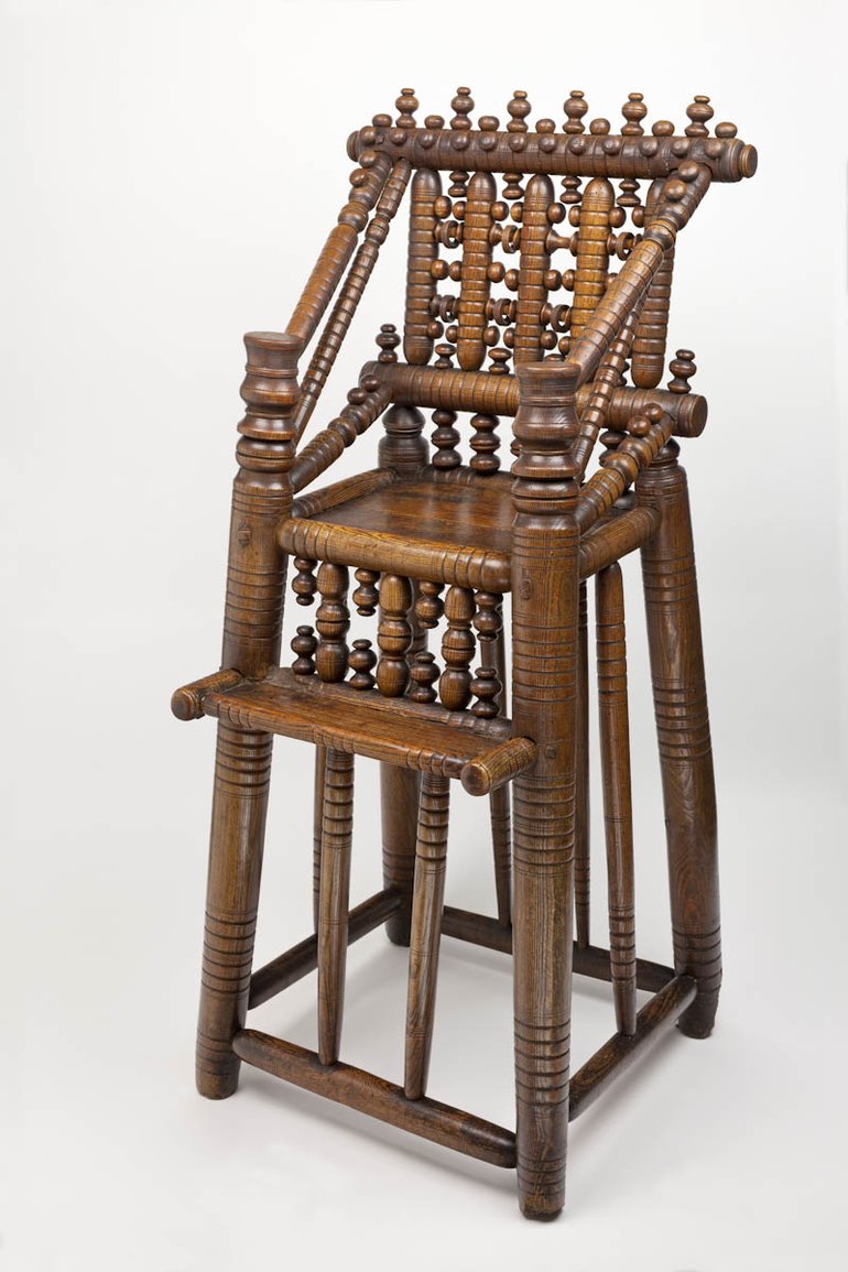 The legs are decorated with patterns of grooves cut round them. There is a platform below the seat for the child's feet, Between the platform and the seat, and at the back of the chair, there is more ornate wood-turning, as there is on the rails at the side running diagonally from the continuation of the front legs to the back.