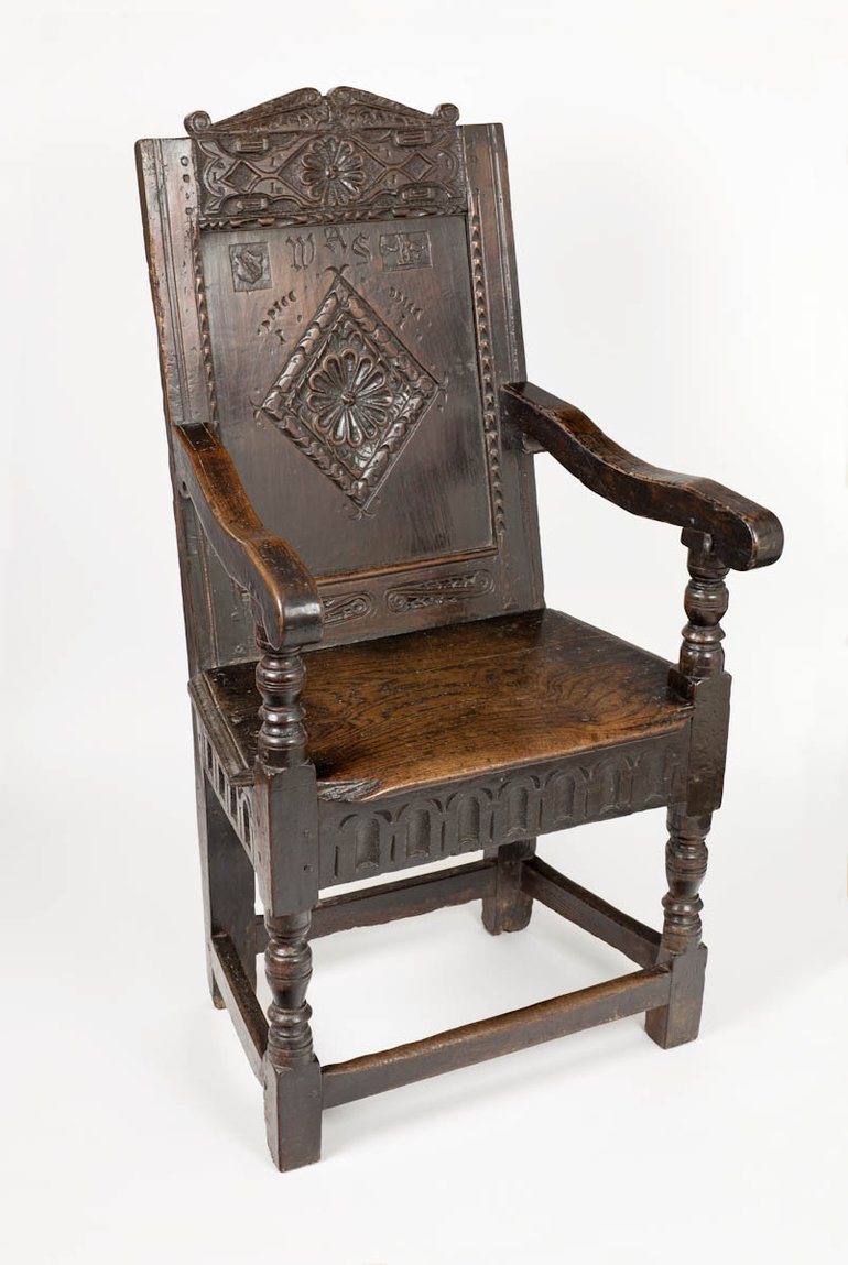 A fairly standard armchair, with turned front legs and a base to the wooden seat which is decorated with carved indentations. The back has a carved diamond decoration, with a flower in the middle, and the (later added) initials are above this. Shakespeare's coat of arms is on a panel at the top  of the back.