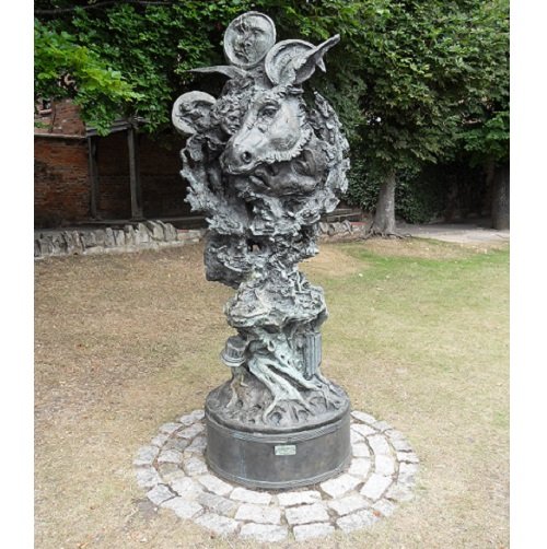 On a circular base, the bronze rises like a twisted tree with figures appearing to clasp it. At the top it widens to a large garlanded ass's head, above which are two circular plaques with faces.