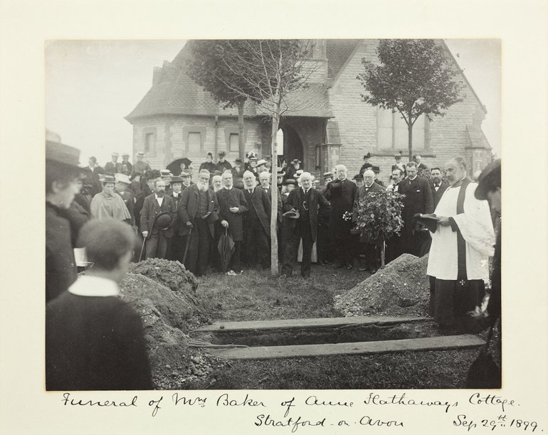 In the foreground is the newly-dug grave with the piles of earth around it; on the right, a clergyman in cassock, surplice and stole is just closing his prayer book. A crowd of formally-dressed people surrounds two sides of the grave, and behind them can be seen the chapel.