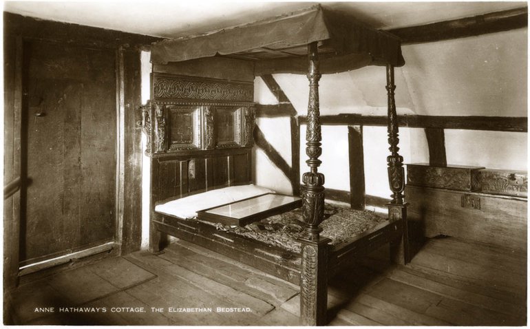 The Hathaway Bed - a four-poster bed with a canopy, with carved posts holding the canopy at the foot, but otherwise very plain. It has a patchwork cover and a white bolster, and in the base the ropes on which the mattress rests are clearly visible. It stand on the bare wooden boards of an empty room, with a wattle and daub wall behind it.