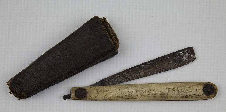 A cased razor; brown leather covered case with two compartments; steel razor with bone handle, two steel rivets hold handle together and form swivel point; scratched on handle the date '1604', the name 'Josh Cols' and the number '2'.