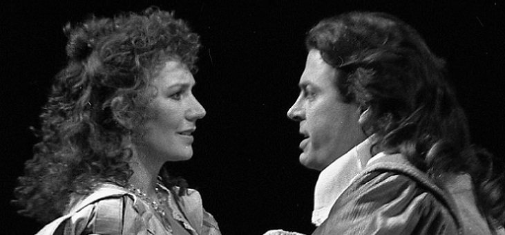 Two characters (Beatrice and Benedick?) stand staring into each other's eyes.