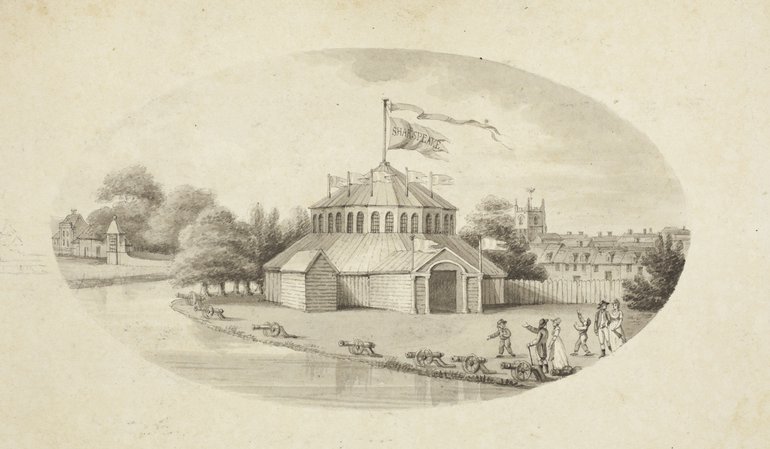 The round building has an entrance extending from it, and a small pitch-roofed building to the left-hand side. The roof of the Rotunda itself (which at the ground floor level is windowless) Rises to a central pavilion with numerous windows. On it are a number of flags, and a flagpole at its peak carries a large flag and above it a long banner.