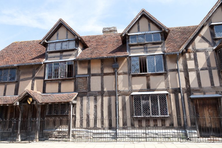 The front of Shakespeare's Birthplace, showing the porch with Shakespeare's arms over the door and the timber frame building with a red-tiled roof with two gable windows.