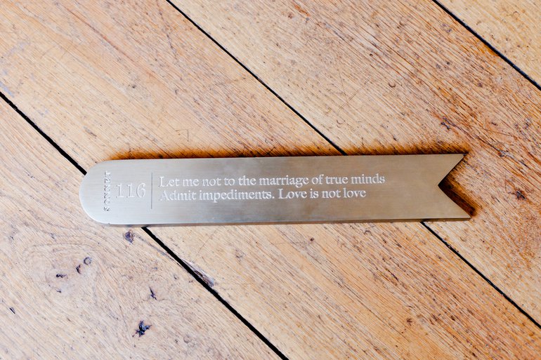 On sanded boards a beige strip shaped like an arrow but with a rounded head has the first two lines from a sonnet:  "Let me not to the marriage of true minds Admit impediment. Love is not love."