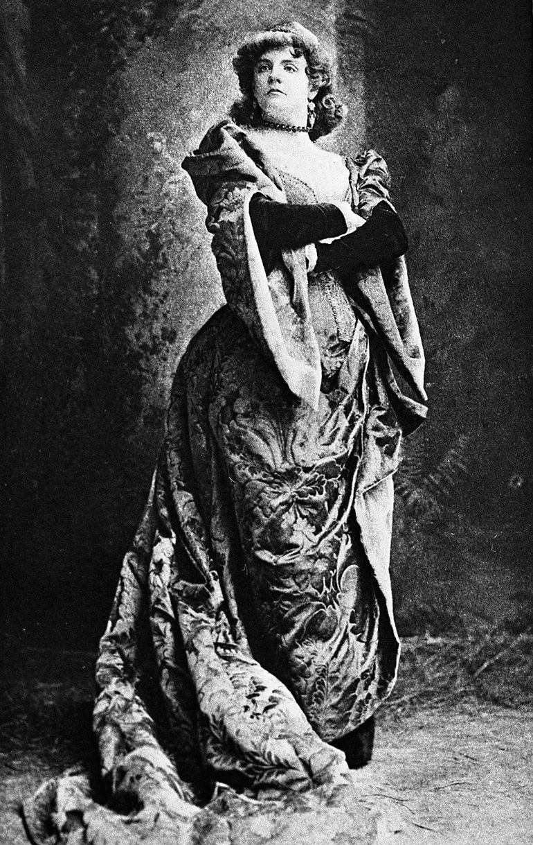 Taming of the Shrew 1888. Ada Rehan. She stands tall and haughty, with her arms folded. She wears a very long, very decorative, robe, the train of which is piled on the floor beside her.