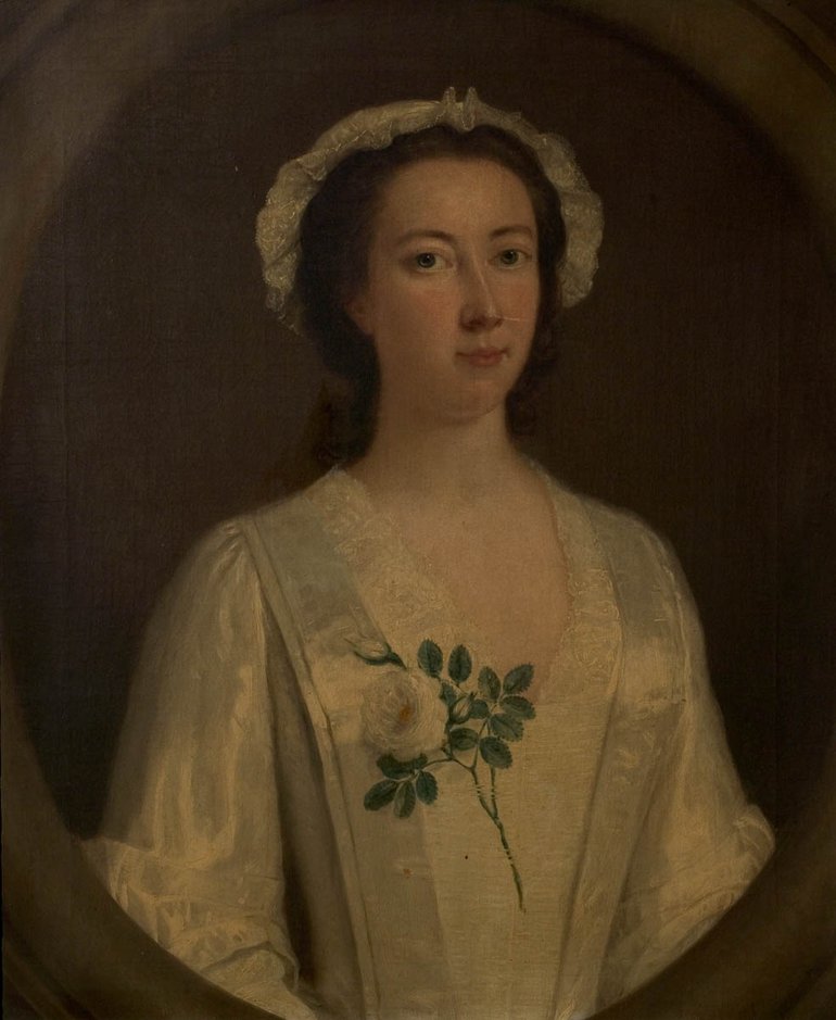 Portrait of an unknown woman in a white dress and cap. She has brown hair and wears a white rose over her right breast.